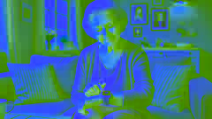 Una mujer anciana usando el dispositivo Memo en una acogedora sala de estar, sonriendo mientras este le ofrece un recordatorio suave.