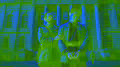 Yu Tsun, menotté, est arrêté par le capitaine Madden devant un grand bâtiment dans la lumière douce du matin.